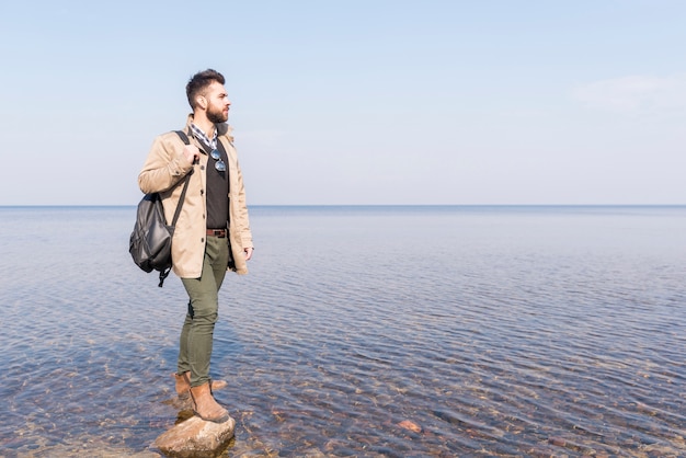 Бесплатное фото Мужской путешественник с его рюкзаком, глядя на идиллическое спокойное озеро