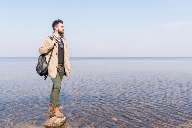 Мужской путешественник с его рюкзаком, глядя на идиллическое спокойное озеро
