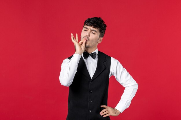 male waiter in a uniform with butterfly on neck and making perfect gesture on red background