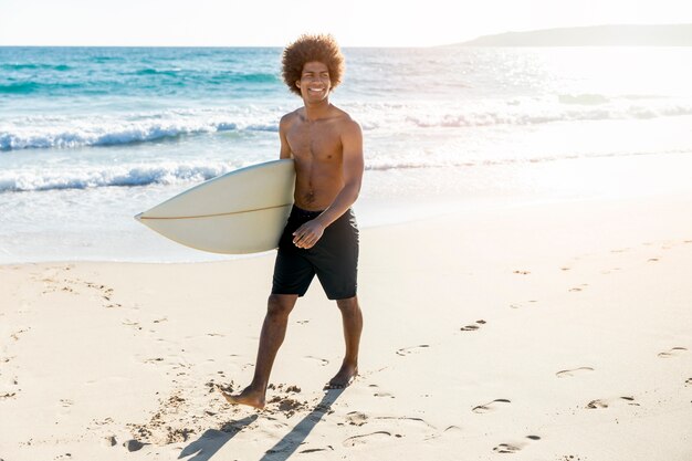 Male walking along beach with surfboard and smiling