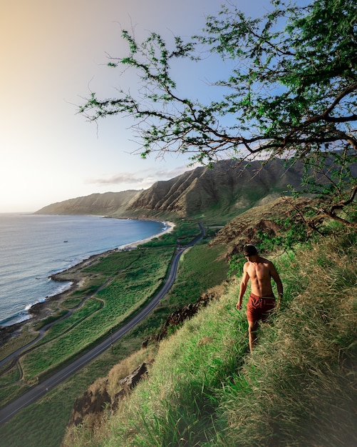 Male walking on a steep green hill with the beautiful sea and hills in the