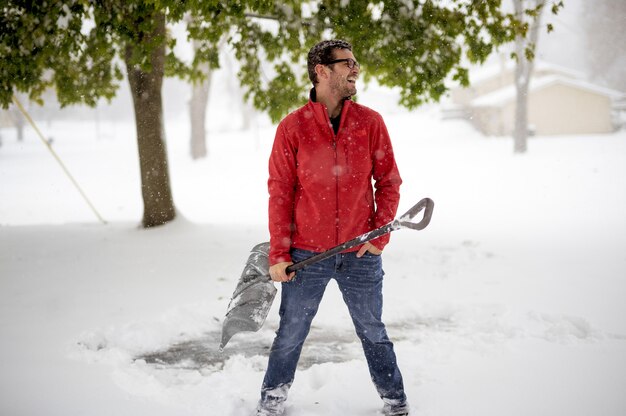 Male wearing a red winter jacket and holding a snow shovel while smiling