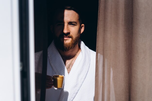Male in white bathrobe with coffee mug in hand.