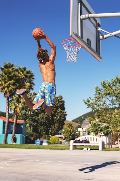 Male with blue and yellow shorts making a dunk in the basketball court during daytime