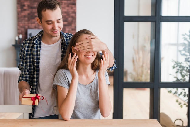 Male with gift closing eyes of woman 