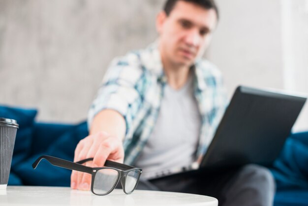 Male with laptop put down glasses on table