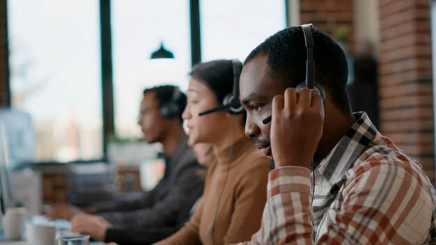 Male worker answering telework phone at call center, using audio headset and microphone. Young man working at customer care in disability friendly office. Handheld shot. Close up.