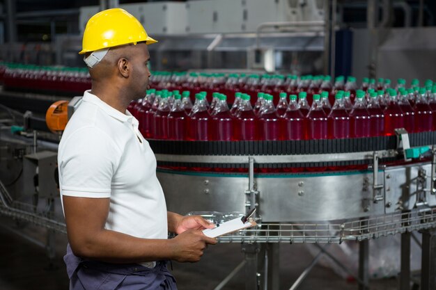 Мужчина-работник осматривает бутылки на фабрике соков