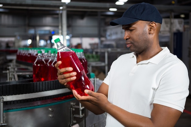 Male worker inspecting juice bottle in factory