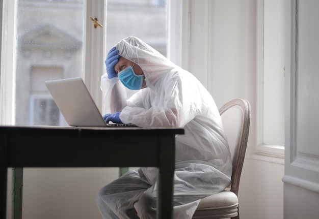 Male works on a computer protected by medical suit and mask