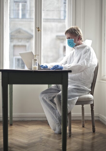 Male works on a computer protected by medical suit and mask