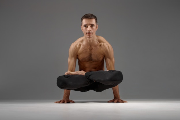 Male yoga keeps balanc on hands in classical pose  meditation position  grey background. strong man doing yogi exercise  asana training  top concentration  healthy lifestyle