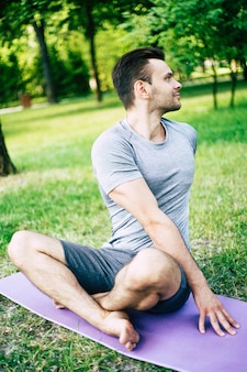 Релаксация мужской йоги. спортивный и стройный красивый молодой человек делает упражнения йоги в городском парке на открытом воздухе. здоровый образ жизни и крепкая душа и тело