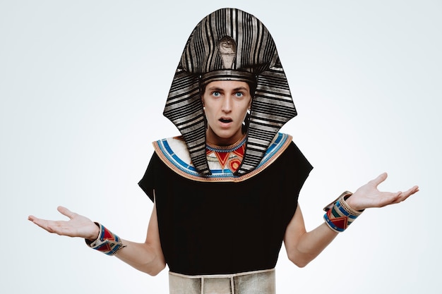 Man in ancient egyptian costume confused raising arms having no answer on white