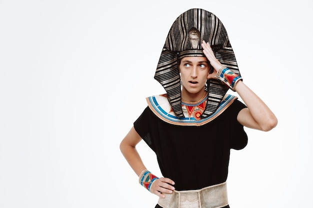 Человек в древнем египетском костюме смотрит в сторону, смущенный, держась за голову на белом