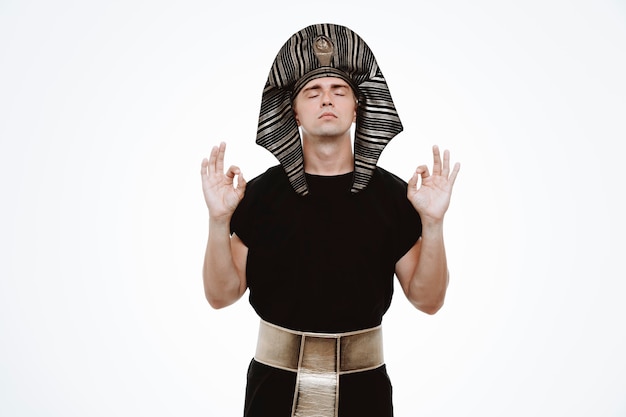 Free photo man in ancient egyptian costume relaxing making meditation gesture with fingers on white