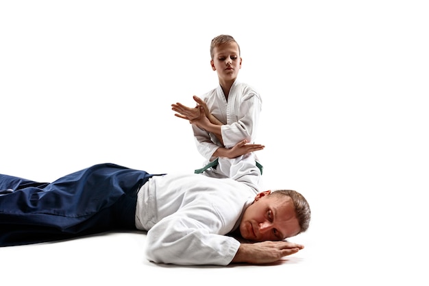 Мужчина и мальчик-подросток борются на тренировках по айкидо в школе боевых искусств. концепция здорового образа жизни и спорта. бойцы в белом кимоно на белой стене. мужчины-каратэ с сосредоточенными лицами в форме.