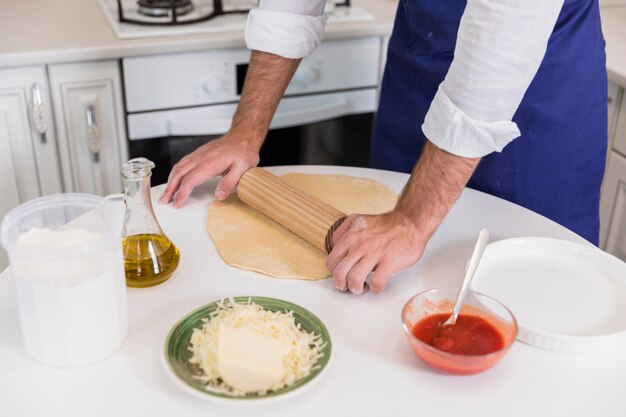Man in apron rolling dough for pizza in kitchen