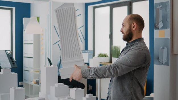 Man architect analyzing building model and maquette to design urban property. Architectural worker designing bleuprints plan and construction layout for modern structure project.
