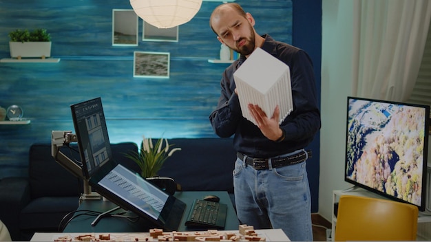 Man architect checking maquette in hand with model on monitor