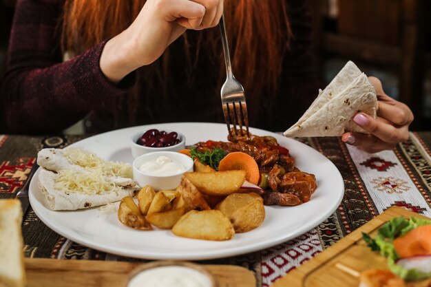 Человек собирается съесть жареную курицу с овощами картофель лаваш сметана лимонад вид сбоку