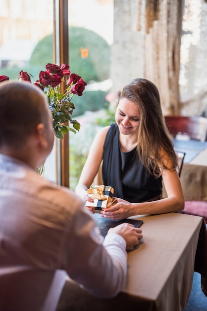 Man and attractive smiling woman with present box at table