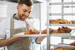 Бесплатное фото Мужчина-пекарь держит круассаны в пекарне