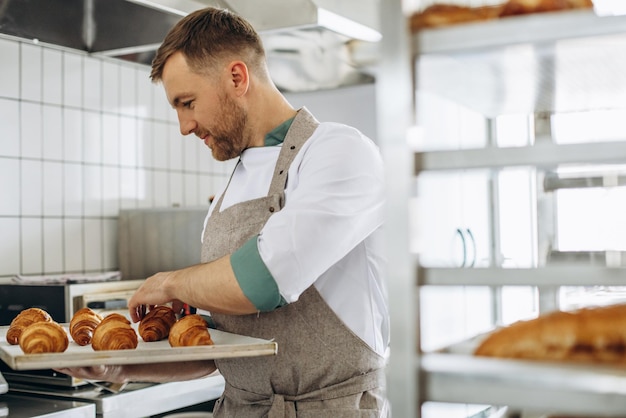 Бесплатное фото Мужчина-пекарь держит круассаны в пекарне