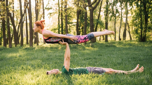 Мужчина балансирует женщину на его во время практики йоги в парке