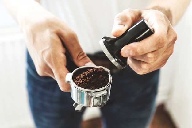 Man barista holding coffee tamper with grind coffee ready for cooking coffee. Closeup