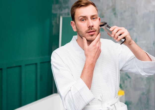 Man in bathrobe using trimmer
