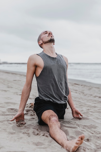 Free photo man on the beach doing the split in yoga routine