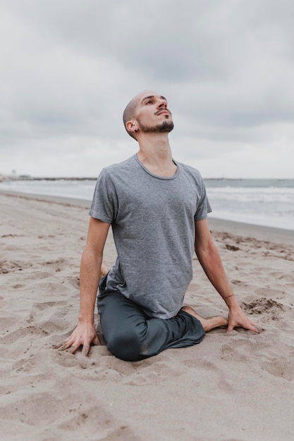 Foto gratuita uomo sulla spiaggia che esercita posizioni yoga