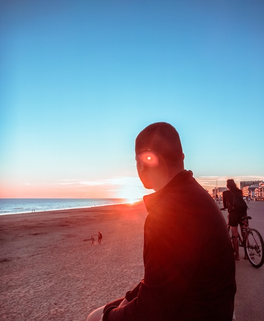 Foto gratuita uomo sulla spiaggia di fronte al sole durante il tramonto