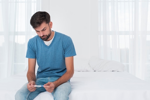 Man in bed holding pregnancy test