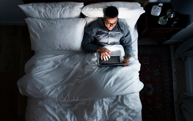 Человек на кровати, используя свой ноутбук
