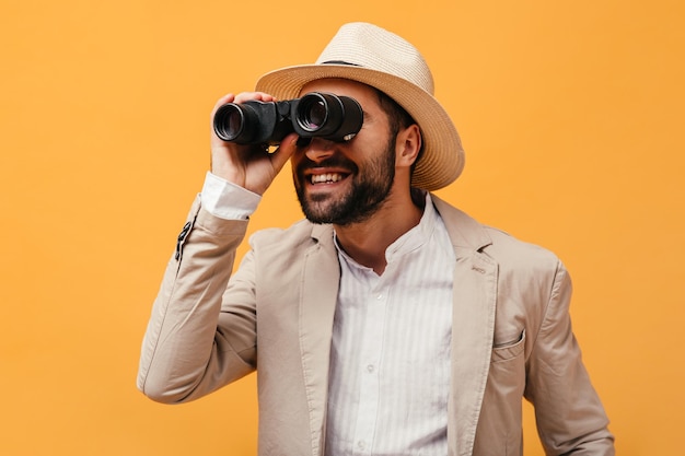 Free photo man in beige hat and jacket looks into binoculars in isolated background