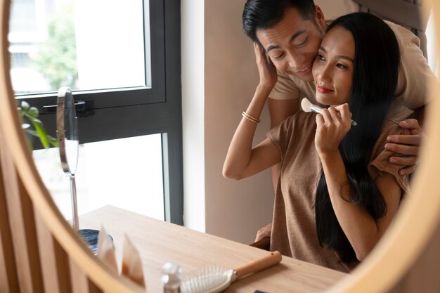 Man being affectionate with woman while she's putting on make-up and looking in the mirror