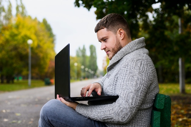 Free photo man on a bench in the park with his laptop