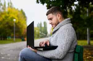 Foto gratuita uomo su una panchina nel parco con il suo computer portatile