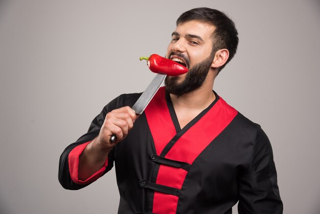 Man biting a red pepper on knife .