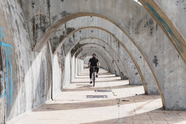 Мужчина в черной одежде едет на велосипеде в арке