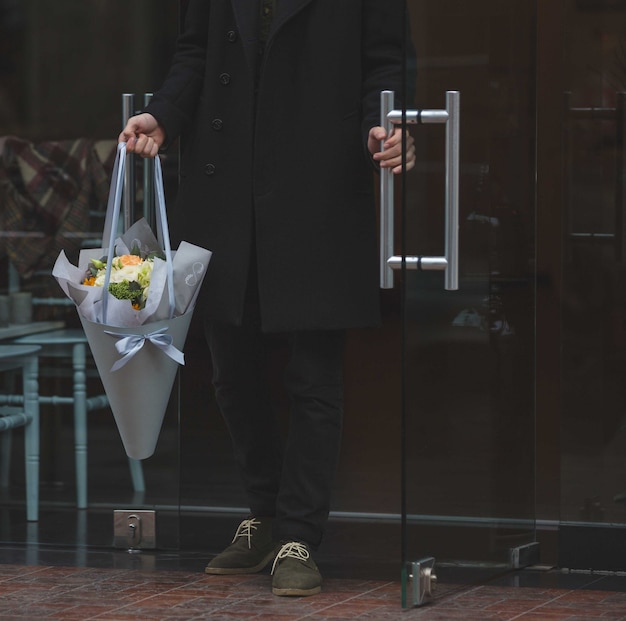 Foto gratuita l'uomo nero vestito entrando con un mazzo bianco di fiori