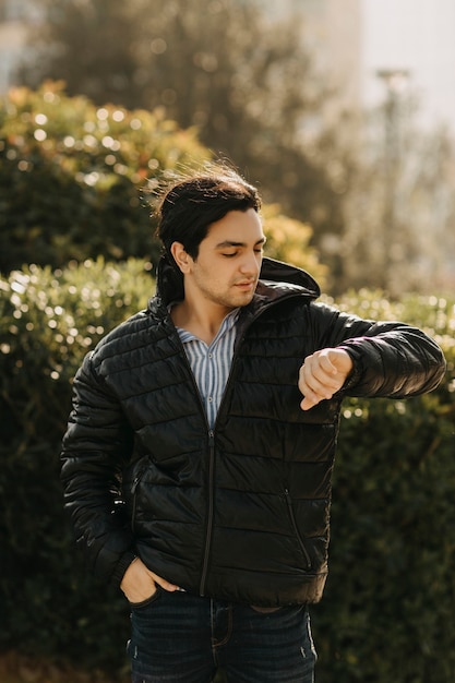 Free photo man in black jacket standing in the park and checking his time. high quality photo