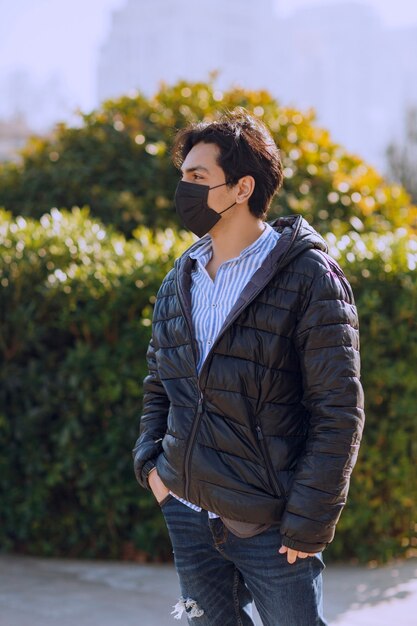 公園を歩いている黒い革のジャケットと黒いフェイスマスクの男。高品質の写真