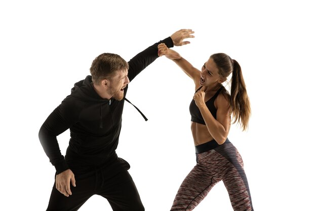 Man in black outfit and athletic woman fighting on white studio wall