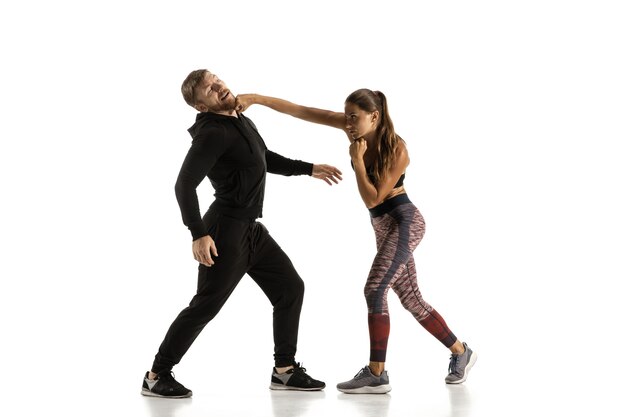 Man in black outfit and athletic woman fighting on white studio wall
