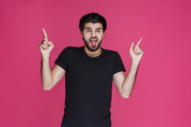 Man in black shirt with beard pointing at something in a confused manner or showing the direction