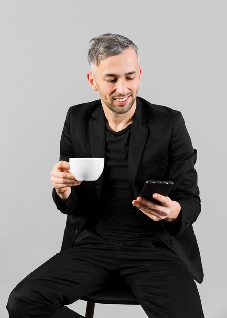 Man in black suit holding a cop and looking at phone