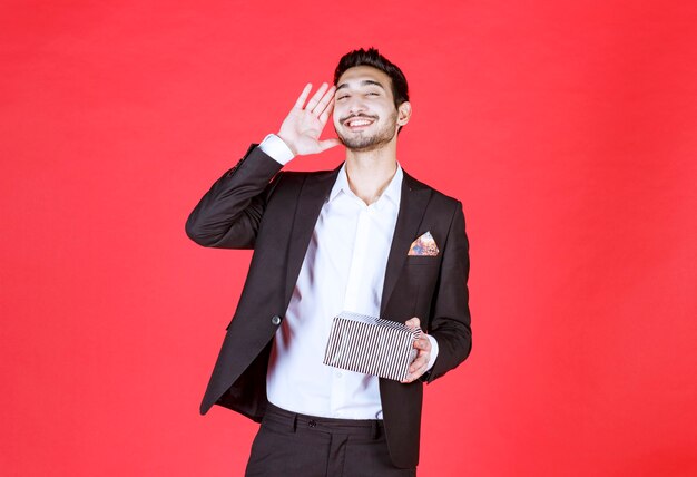 Man in black suit holding a silver gift box.